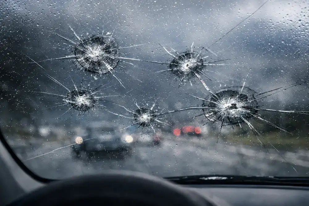 Windshield with several chips and spreading cracks viewed from inside a car, showing how small impacts can expand and weaken the glass.