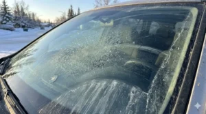 Cracked windshield damaged by road salt and sand during Anchorage Alaska winter driving conditions
